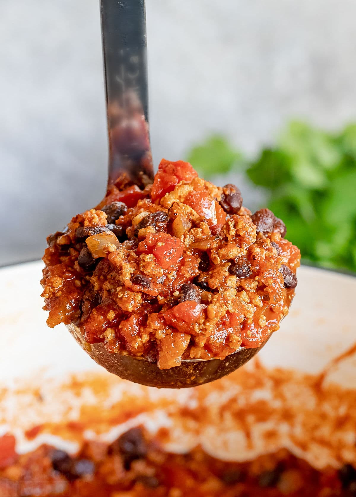 ladle of chili being held up above the pot.