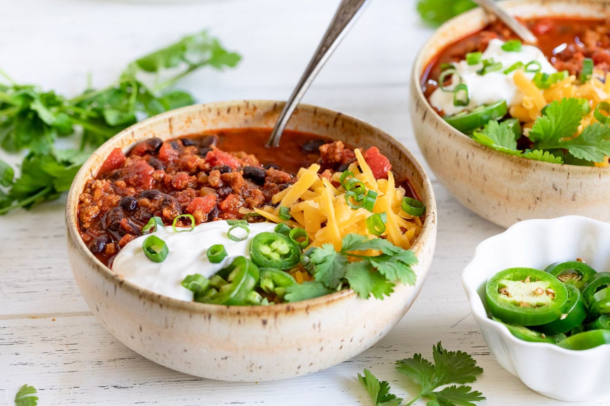 two bowls of chili loaded with toppings.