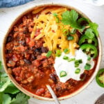 bowl of turkey chili with cheddar cheese sour cream cilantro and green onions.