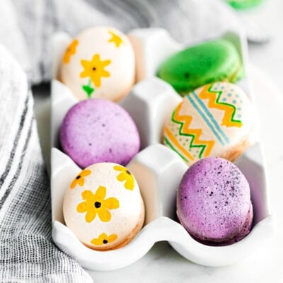 french macarons decorated as easter eggs sitting in white egg crate.