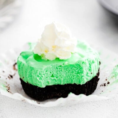grasshopper mini cheesecake unwrapped with whipped cream on top and sitting on white surface