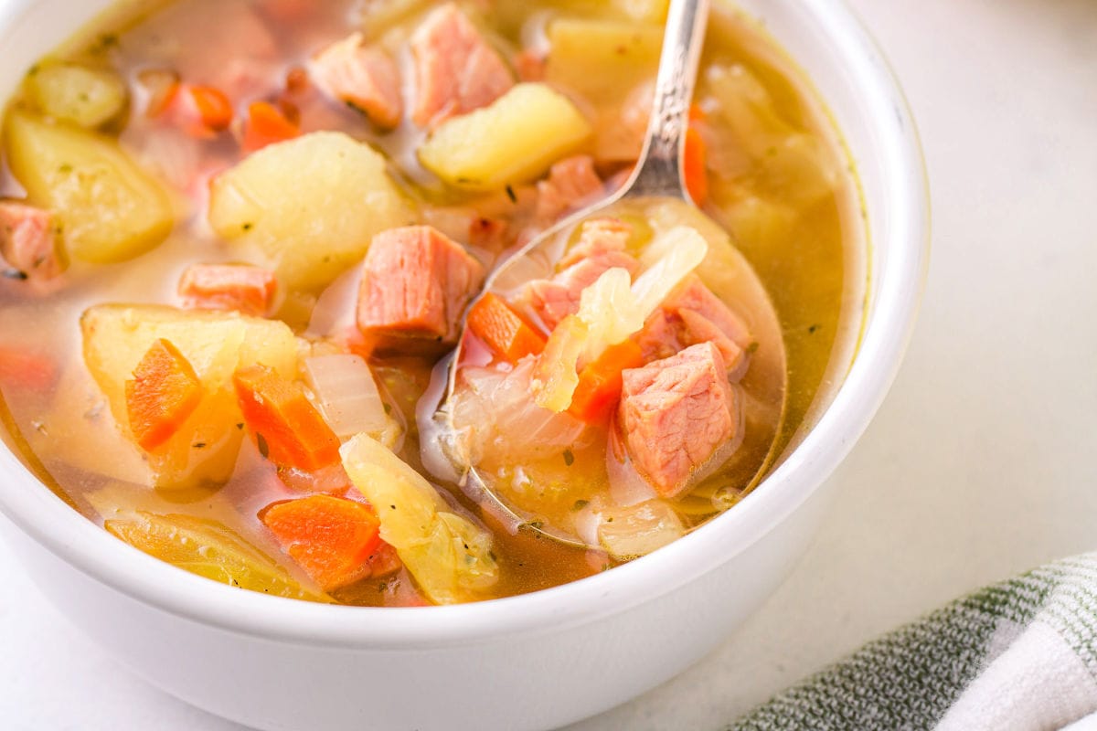 spoon in bowl filled with cabbage and ham soup.