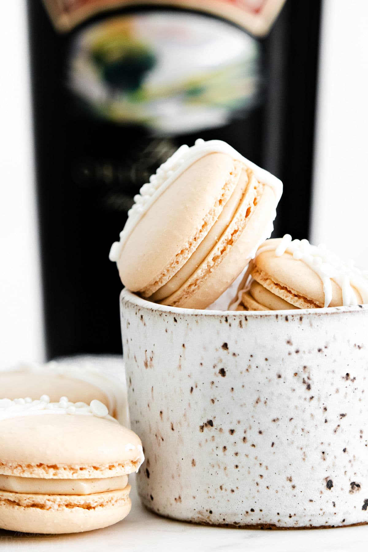 macarons with a creamy Irish cream filling in small white bowl with bottle of Bailey's Irish cream in background.