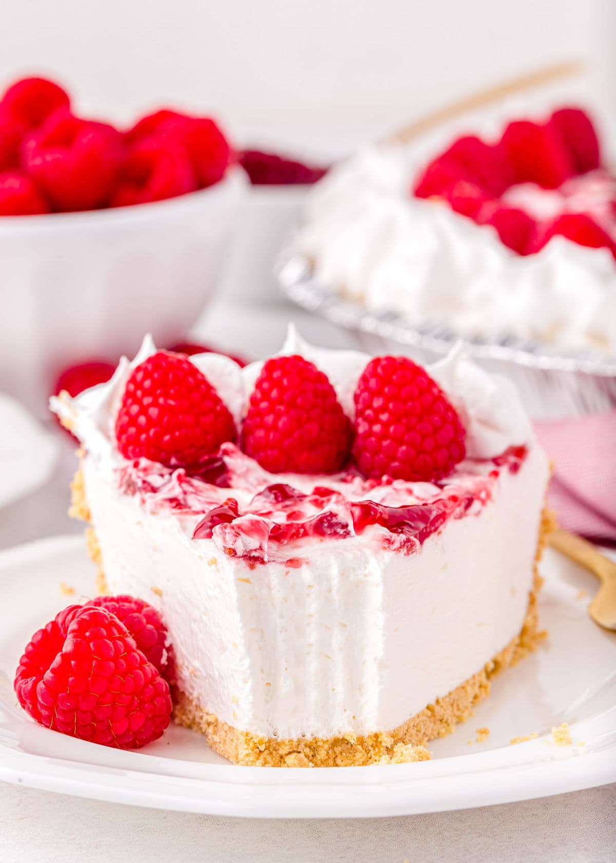 piece of raspberry no bake cheesecake with bite taken sitting on white plate and garnished with fresh raspberries.