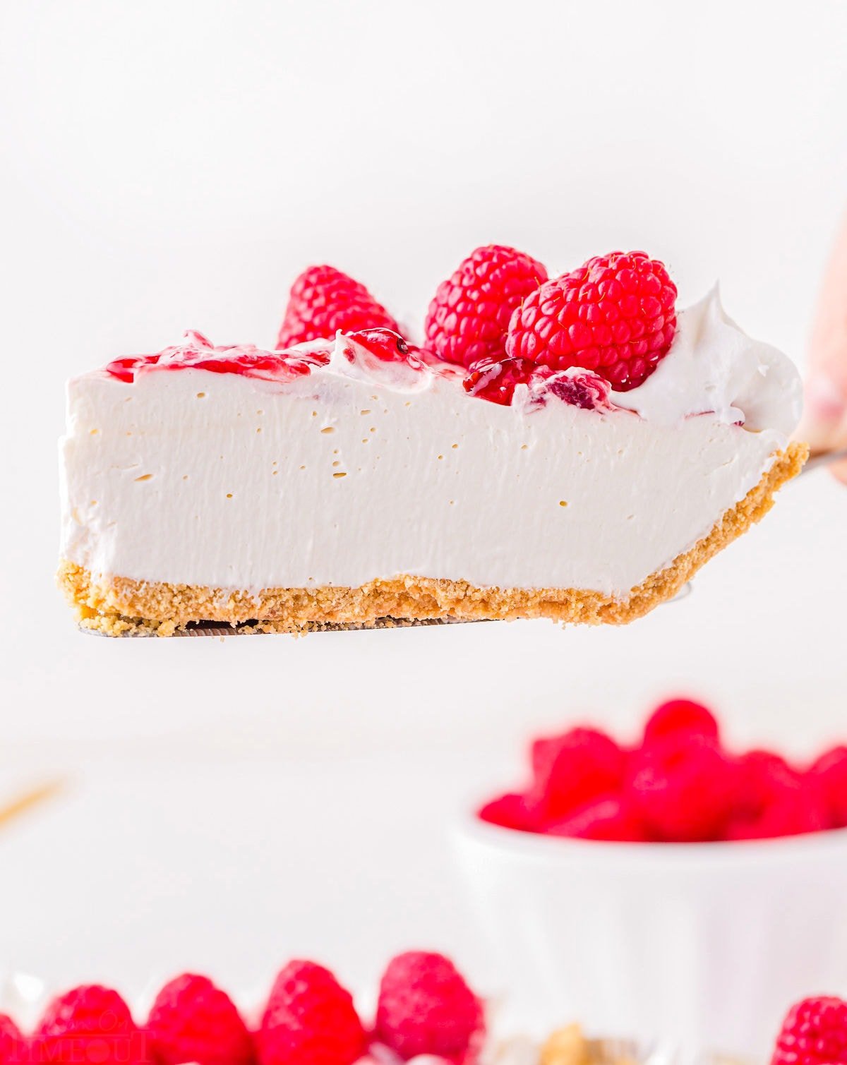 slice of cheesecake with raspberries being held up over pie plate.