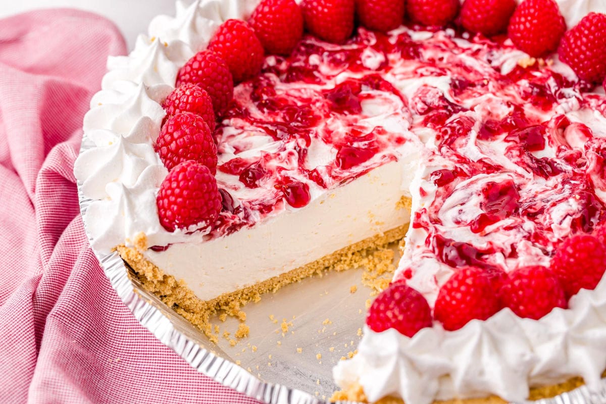 whole raspberry cheesecake with just 1 slice removed sitting next to pink towel.