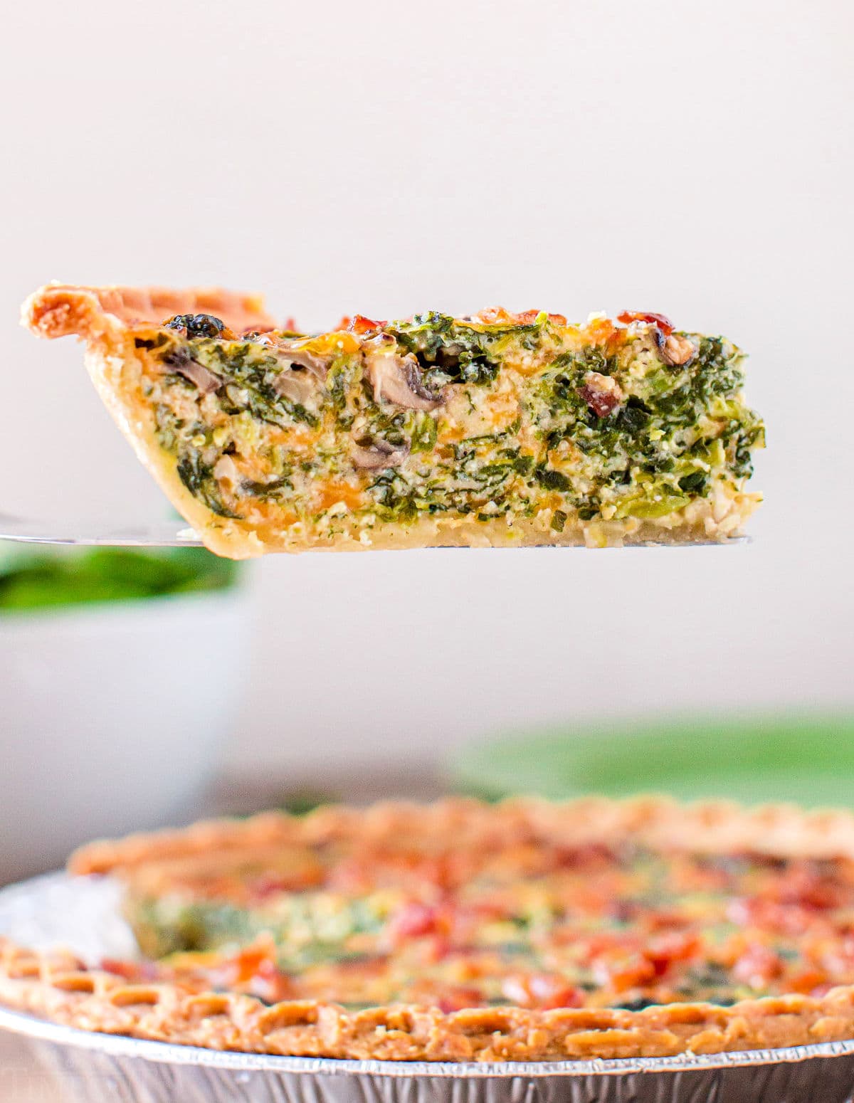 slice of spinach mushroom quiche held up over pie plate.