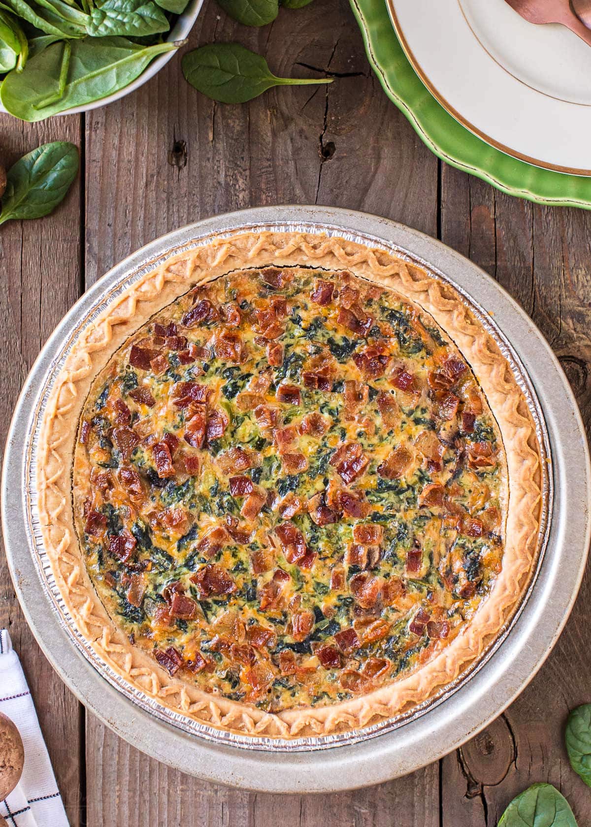 top down view of whole spinach quiche on wood surface.