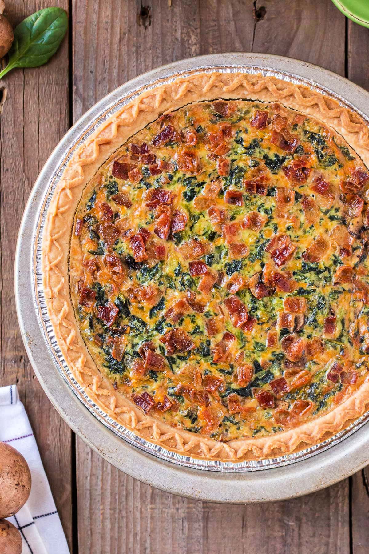 top down view of whole spinach quiche sitting on wood surface.