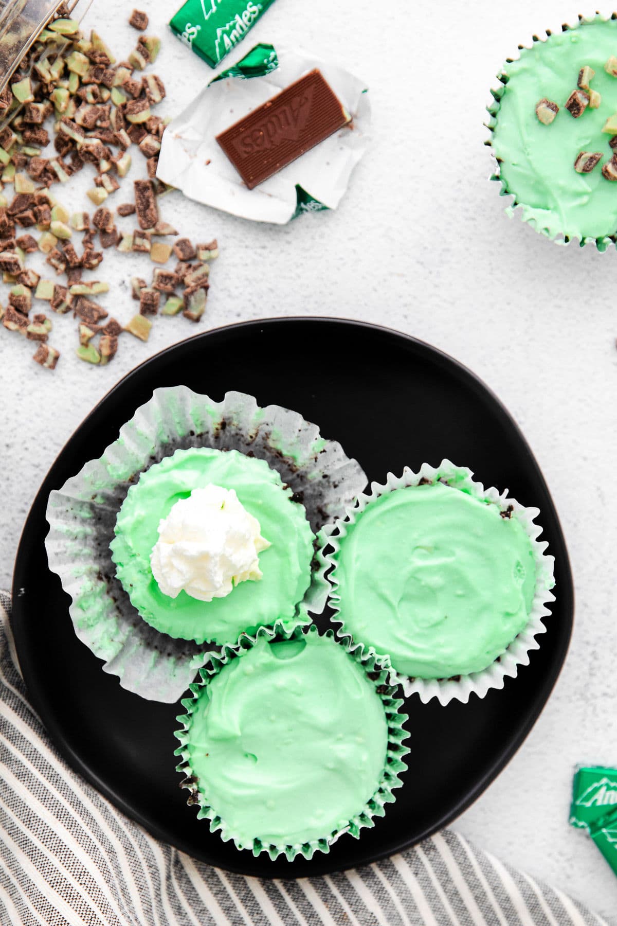 top down look at green mini cheesecakes on a black plate one topped with whipped cream.