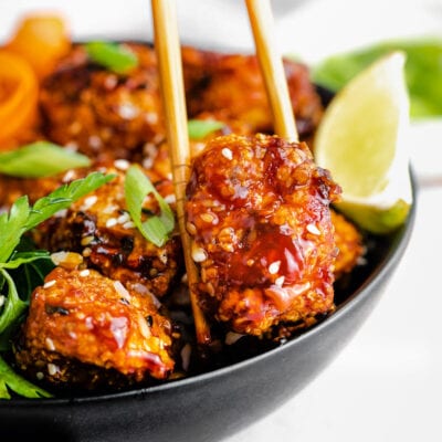 piece of teriyaki chicken being picked up out of a bowl with chopsticks.