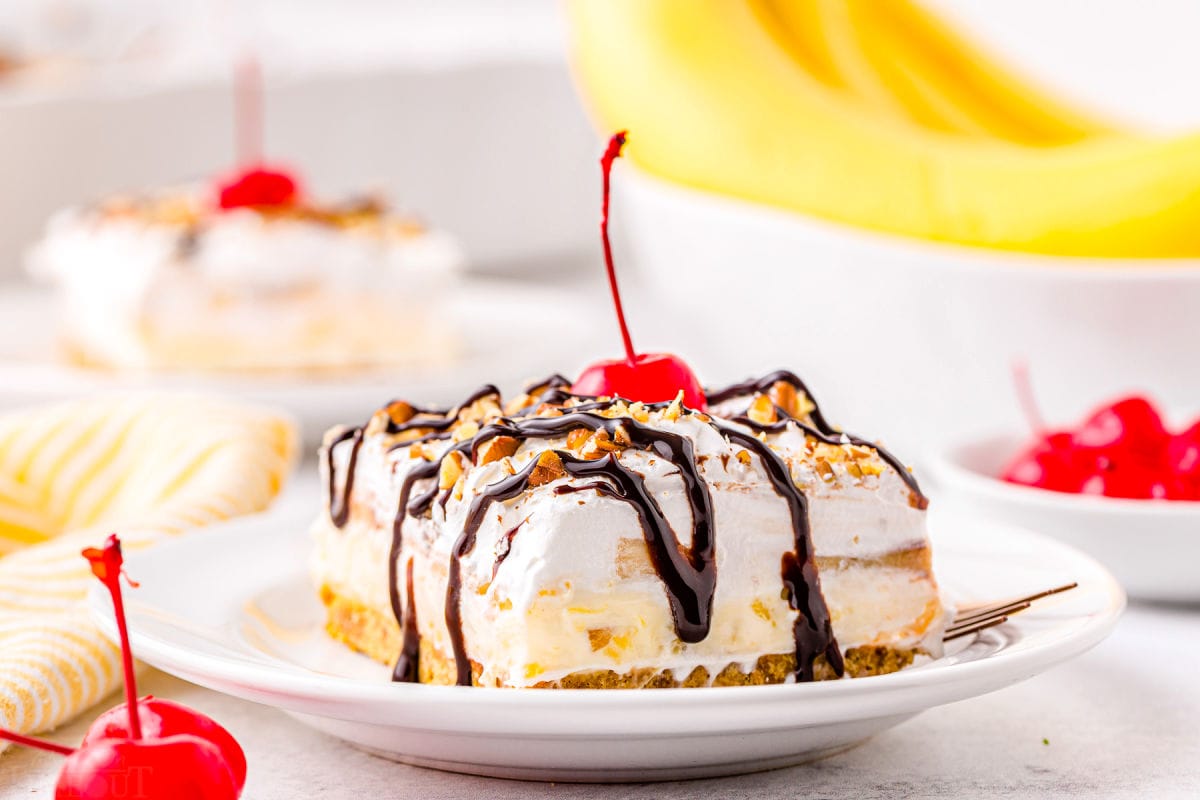 layered banana dessert with pineapple, bananas, and a graham cracker crust. plated on a white plate and topped with a cherry.