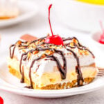 banana split no bake dessert on white plate topped with chocolate sauce and a cherry.