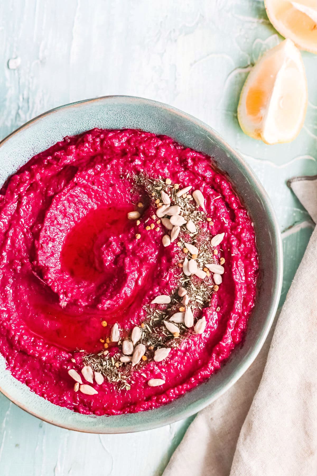 hummus made with roasted beet in blue bowl topped with seeds and oil.