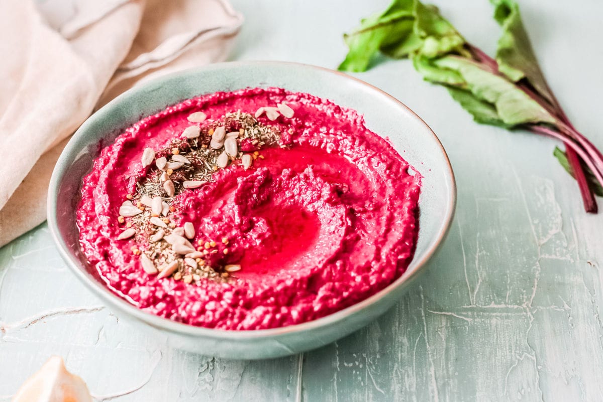 easy beet hummus in large blue green bowl garnished with seeds and oil and finished with a swirl.