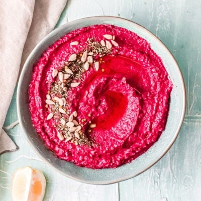 beet hummus in a light blue bowl with a beige napkin to the side.