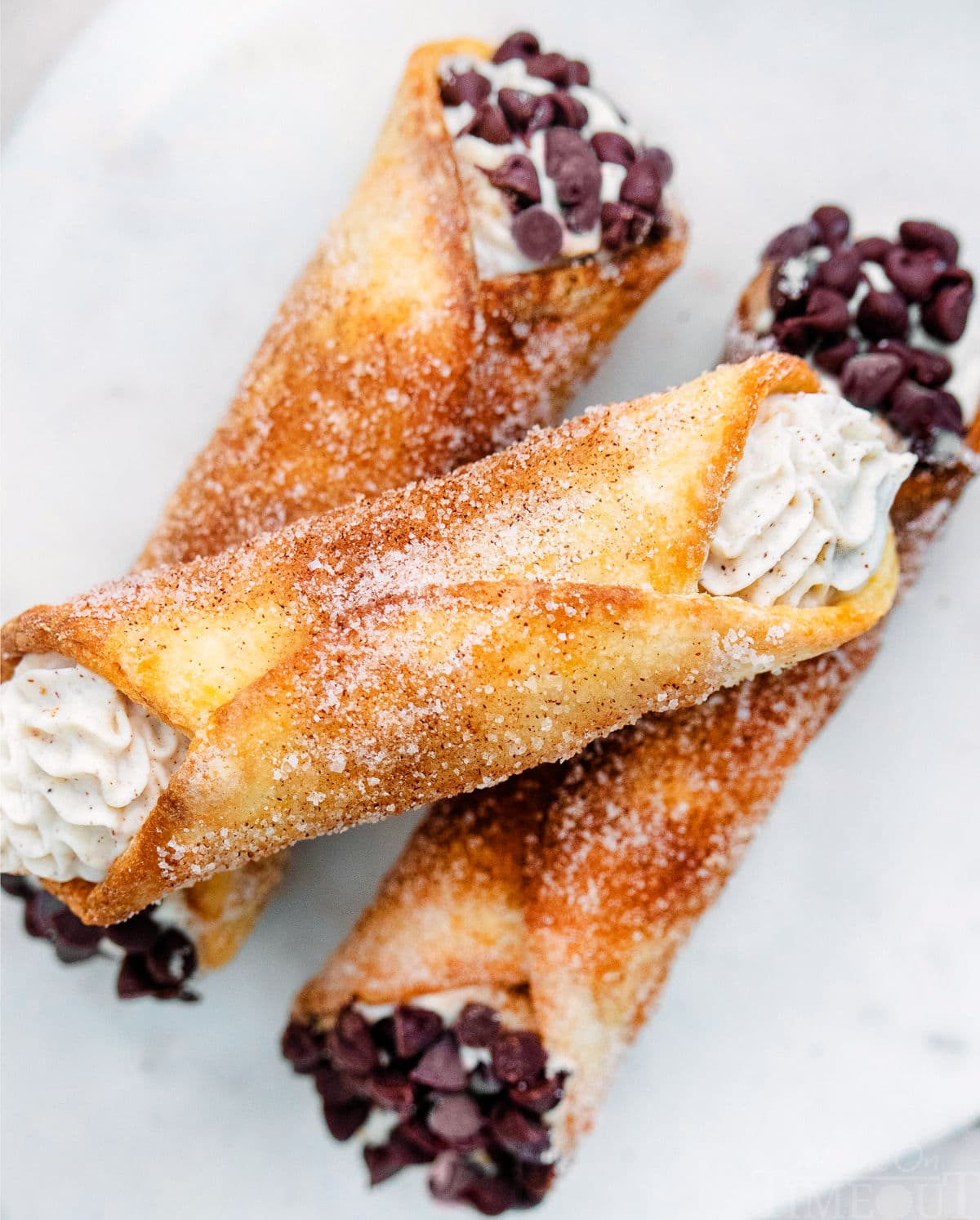 close up look at cannolis with a churro coating. three stacked on a white plate.