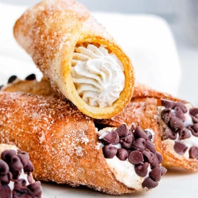 three cannolis sitting on white plate with cannoli filling and chocolate chips.