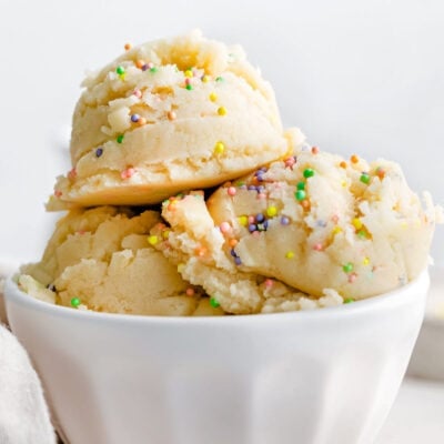 three scoops of cookie dough in white ice cream cup topped with sprinkles.