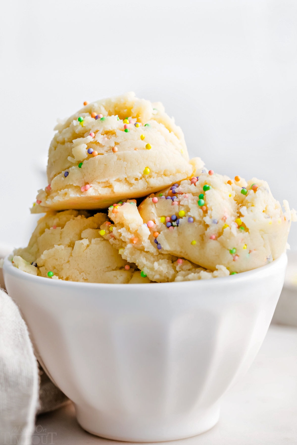 three scoops of cookie dough in white ice cream cup topped with sprinkles.