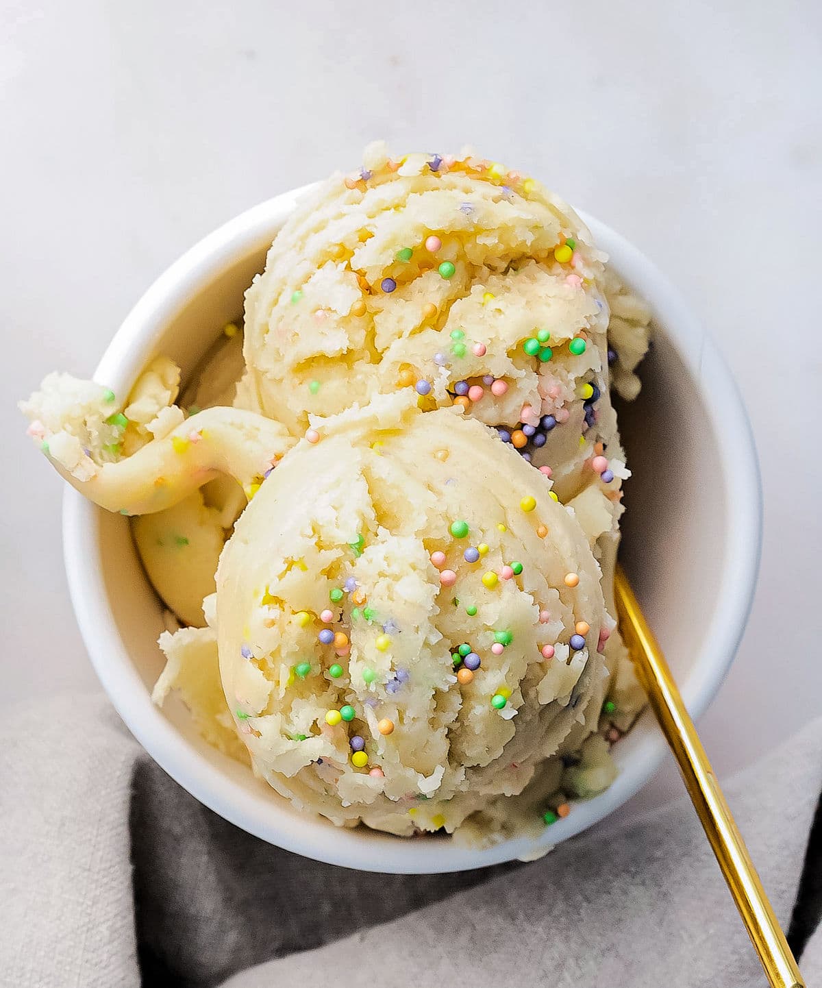 top down look at cookie dough with sprinkles in small white bowl with gold spoon.