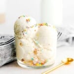 homemade vanilla ice cream scooped into a small glass container with gold spoon lying next to it.