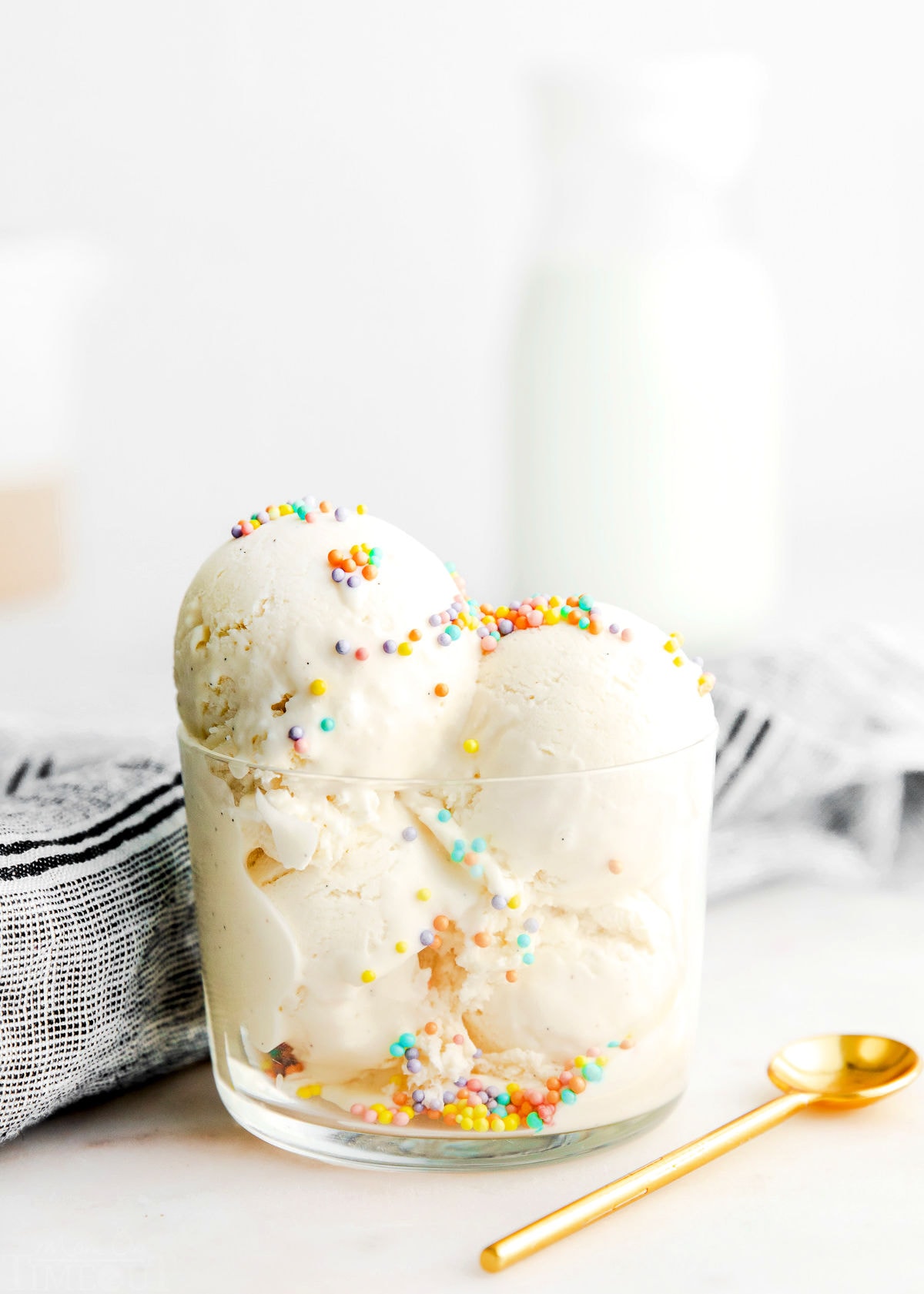 homemade vanilla ice cream scooped into a small glass container with gold spoon lying next to it.