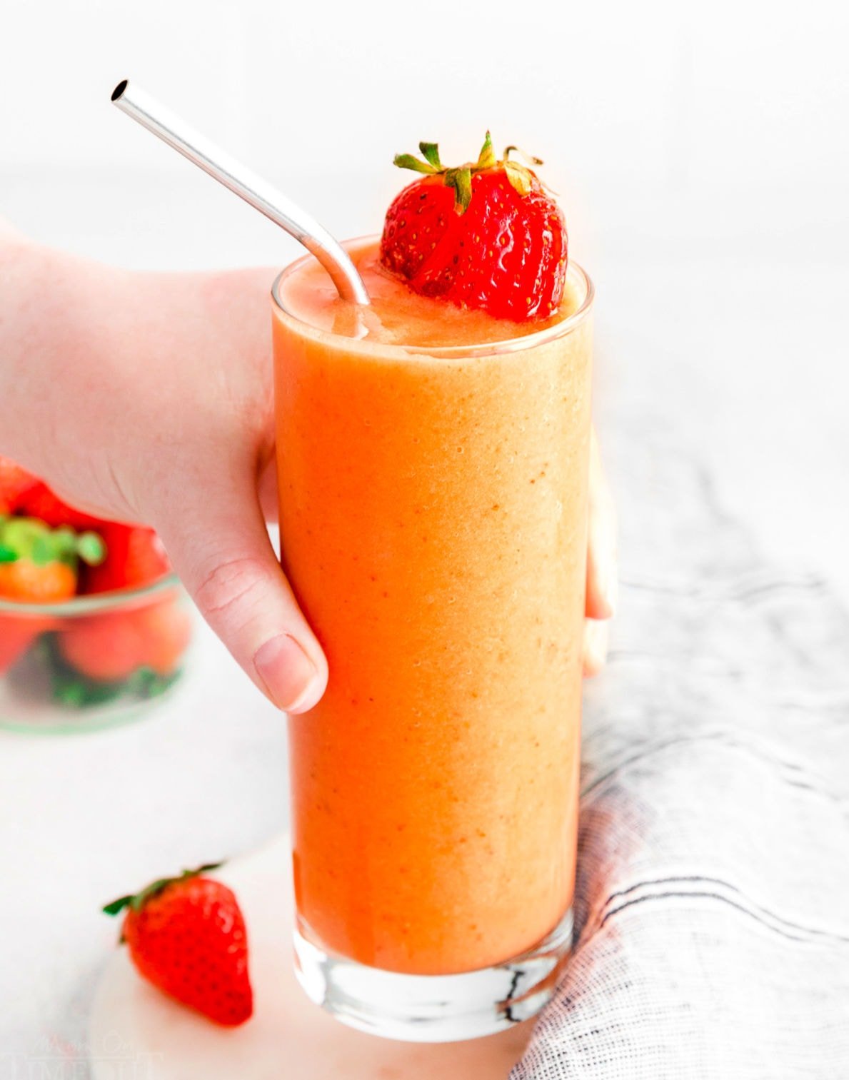 hand picking up smoothie in glass garnished with a sliced strawberry.