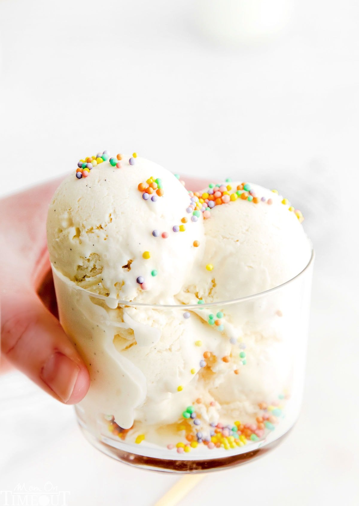 hand holding glass filled with ice cream and topped with colorful sprinkles.