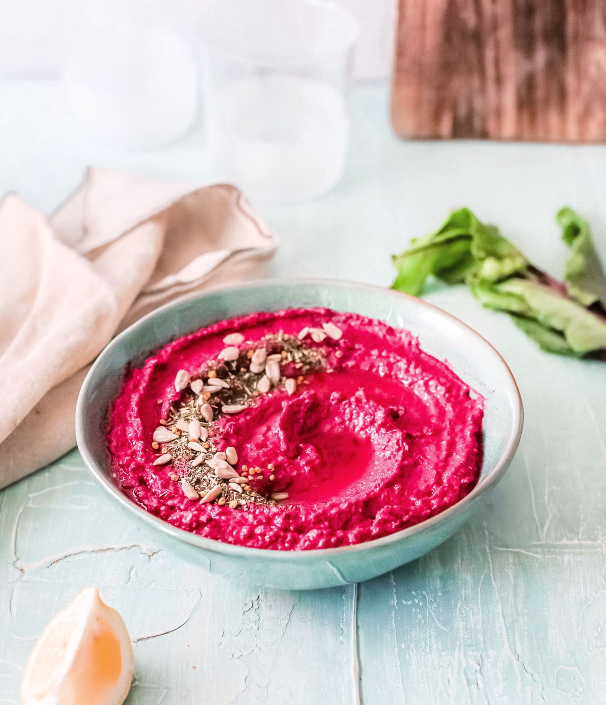 roasted beet hummus in bowl topped with seeds and oil. beige towel and wood board in background.