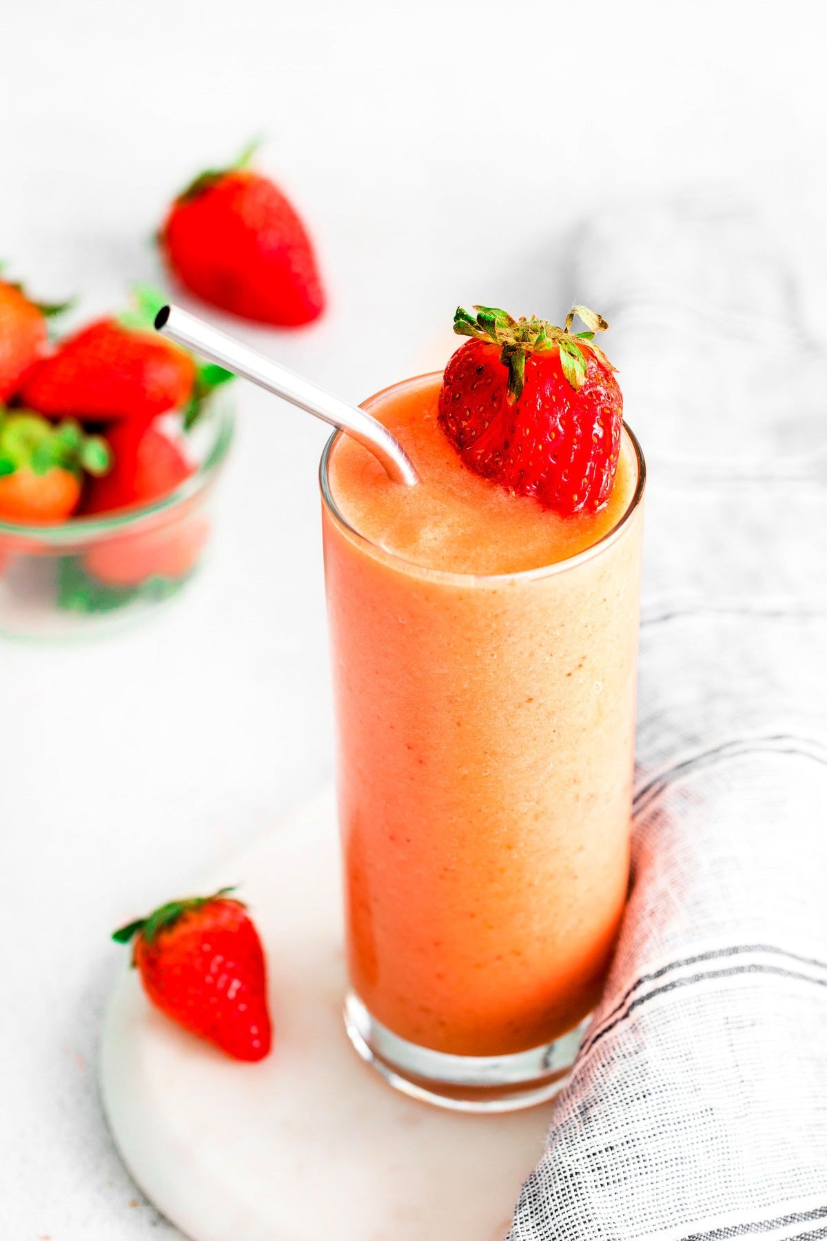 strawberry smoothie with mango in a tall glass on white surface.