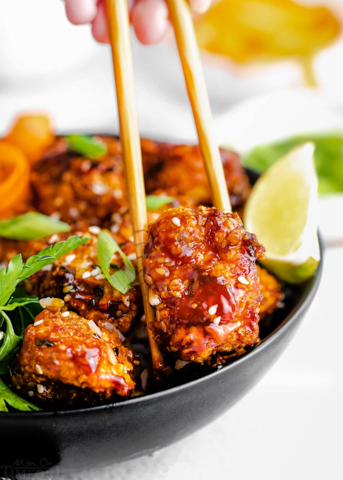 piece of teriyaki chicken being picked up out of a bowl with chopsticks.