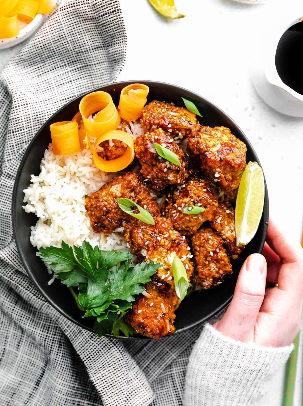 black bowl with rice and teriyaki chicken garnished with orange peels, lime wedge and parsley.