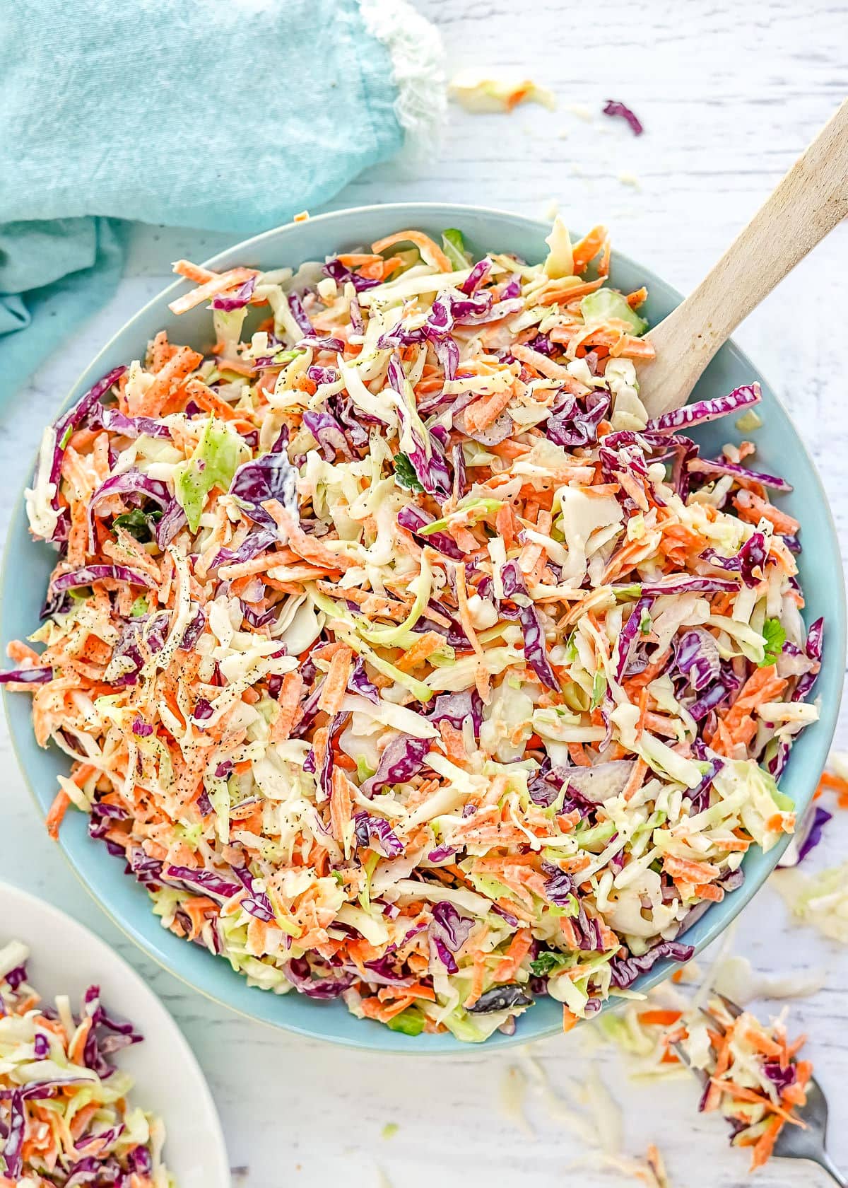 coleslaw prepared in a light blue bowl with wood spoon in the bowl.