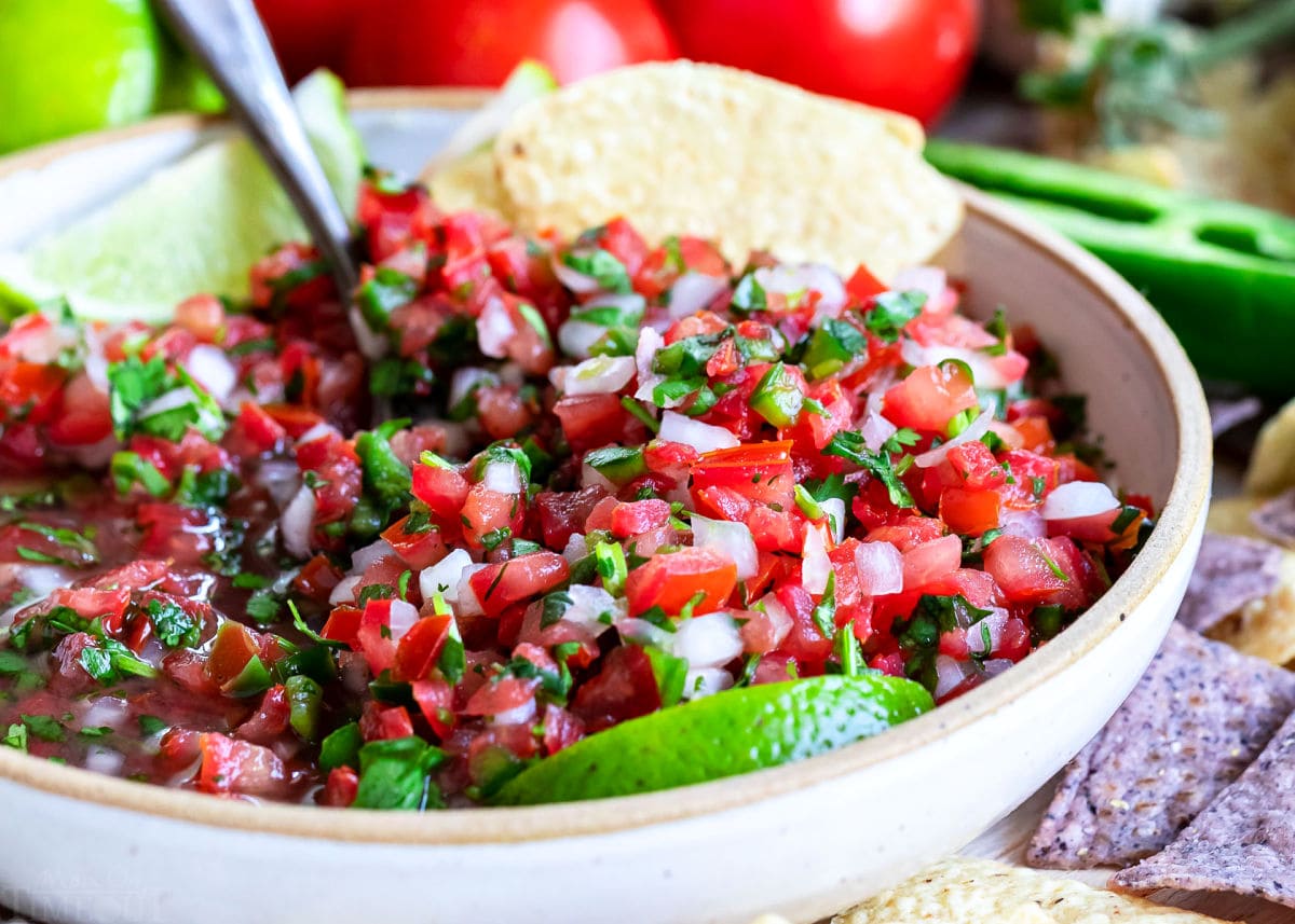 close up look at pico de gallo all mixed up in a medium sized clay bowl with chips around it.  