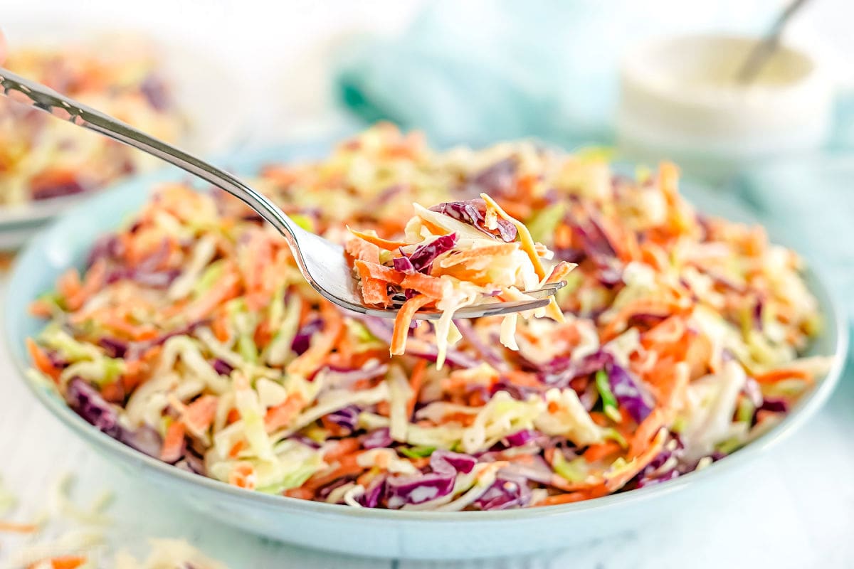 forkful of coleslaw held in front of large bowl with coleslaw in it.