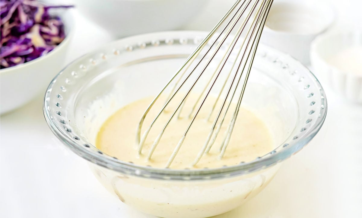 coleslaw dressing in glass bowl with whisk.