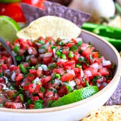 beautiful salsa in white bowl with lime wedges and tortilla chips.