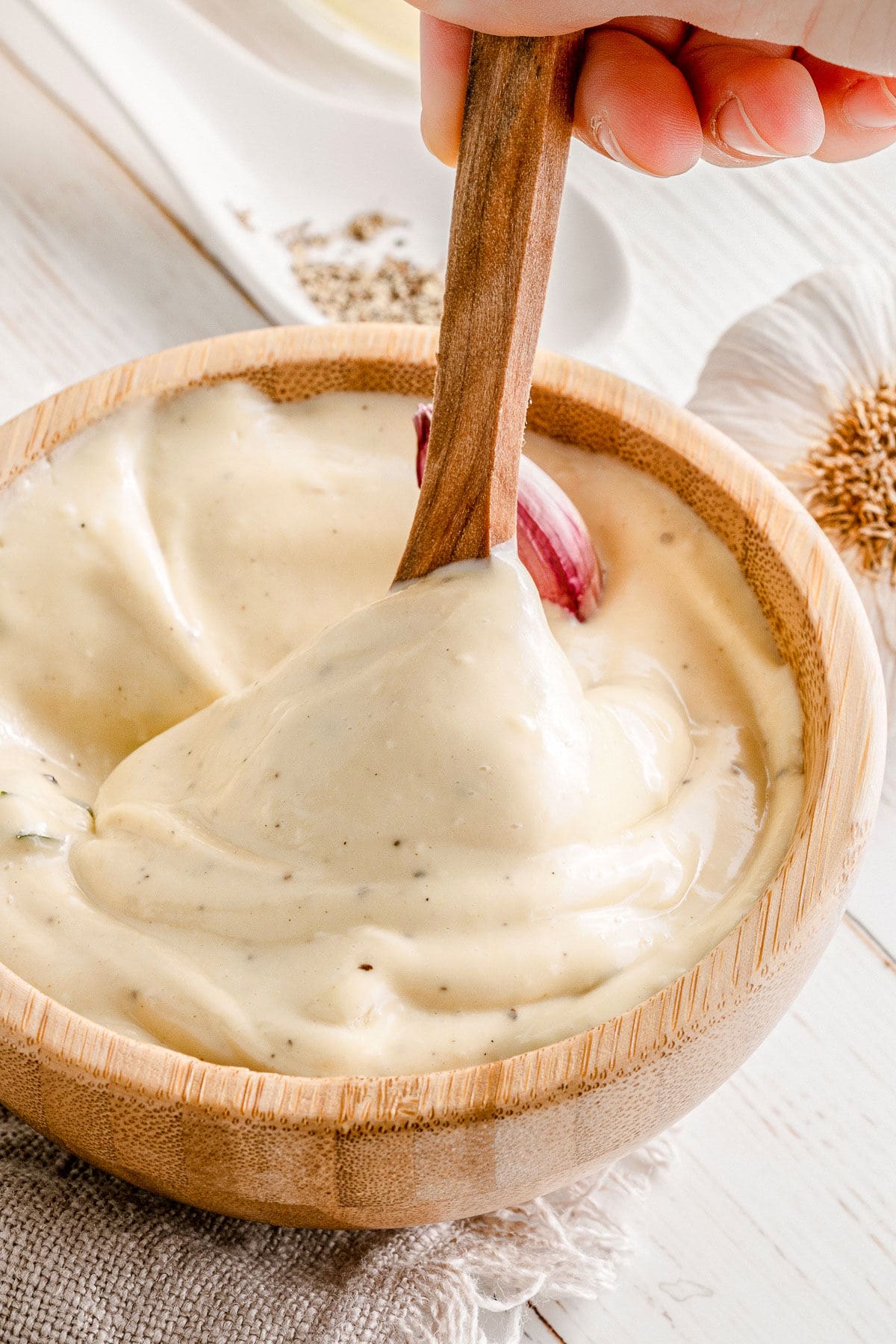 spoon dipped in aioli sauce in a small wood bowl.