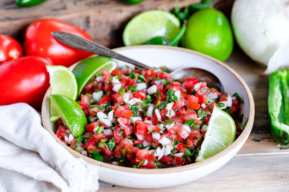 salsa fresco or pico de gallo in bowl ready to be enjoyed with ingredients behind it.