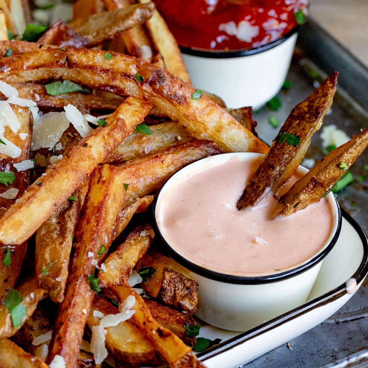 overhead look at two fries dunked in fry sauce sitting on a plate filled with oven fries.