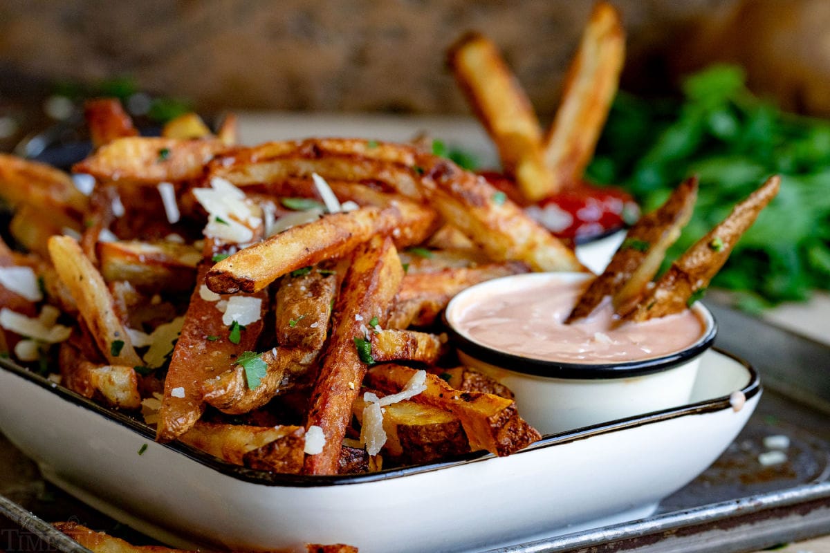 wide shot of french fries in white dish with dipping sauce.