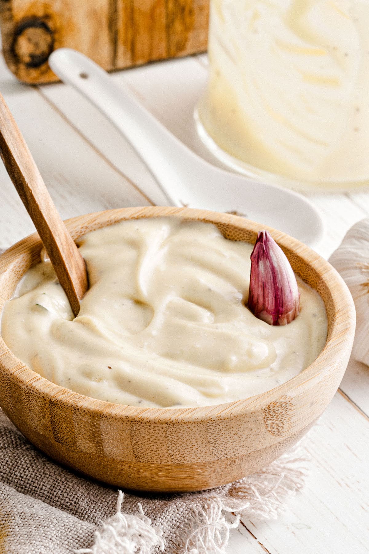 garlic aioli served in wood bowl with spoon inserted and garlic clove resting on top of aioli.