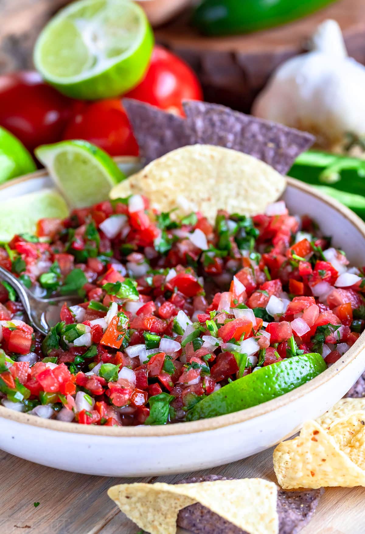 bowl of salsa fresca with some removed. spoon and a few chips are in the bowl.