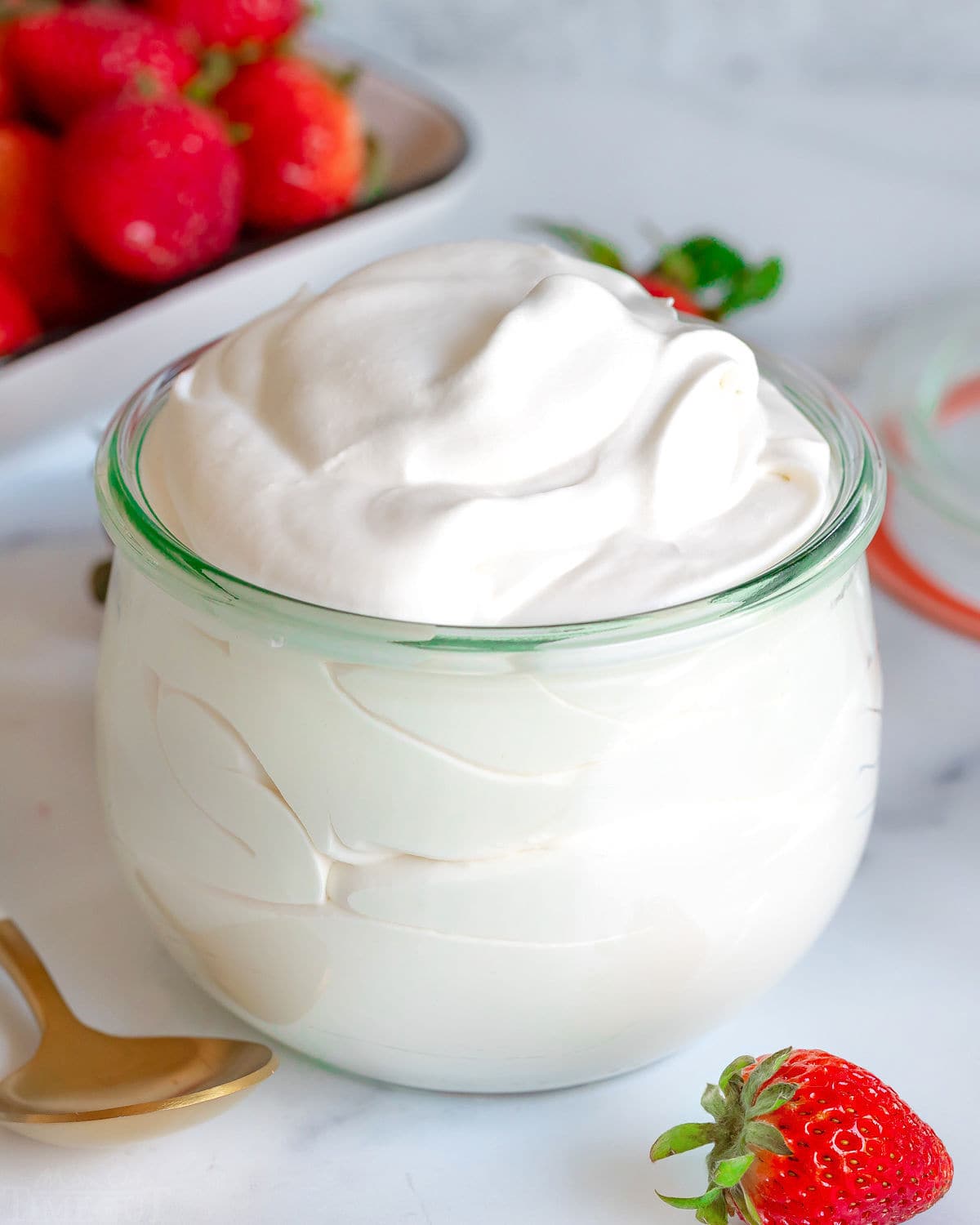 fluffy whipped cream in large weck jar with fresh strawberries scattered about.
