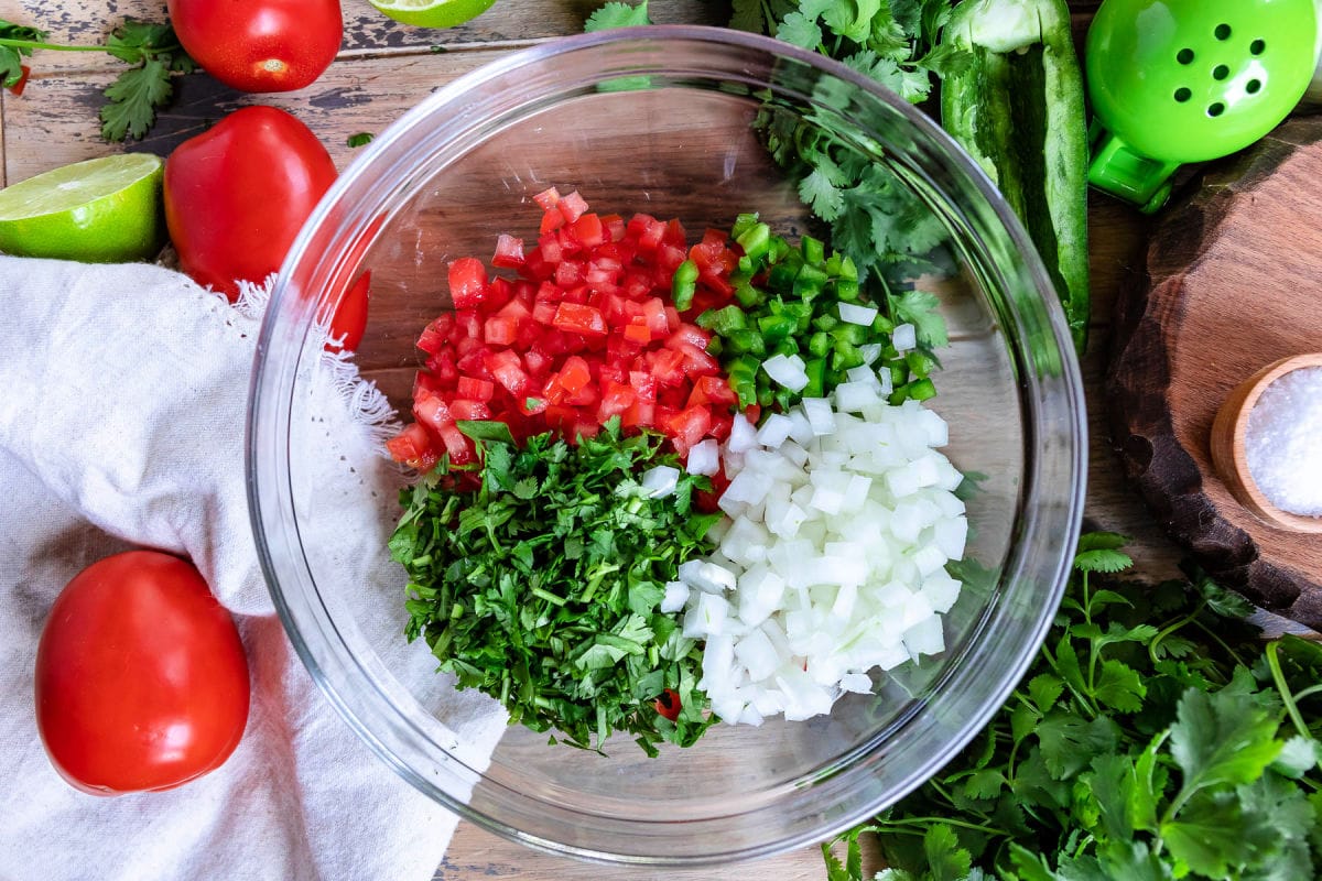 tomatoes, cilantro, jalapeno, and onion chopped up and added to clear glass bowl.