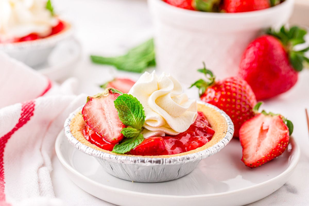 small strawberry pie topped with cream and mint on a white plate.