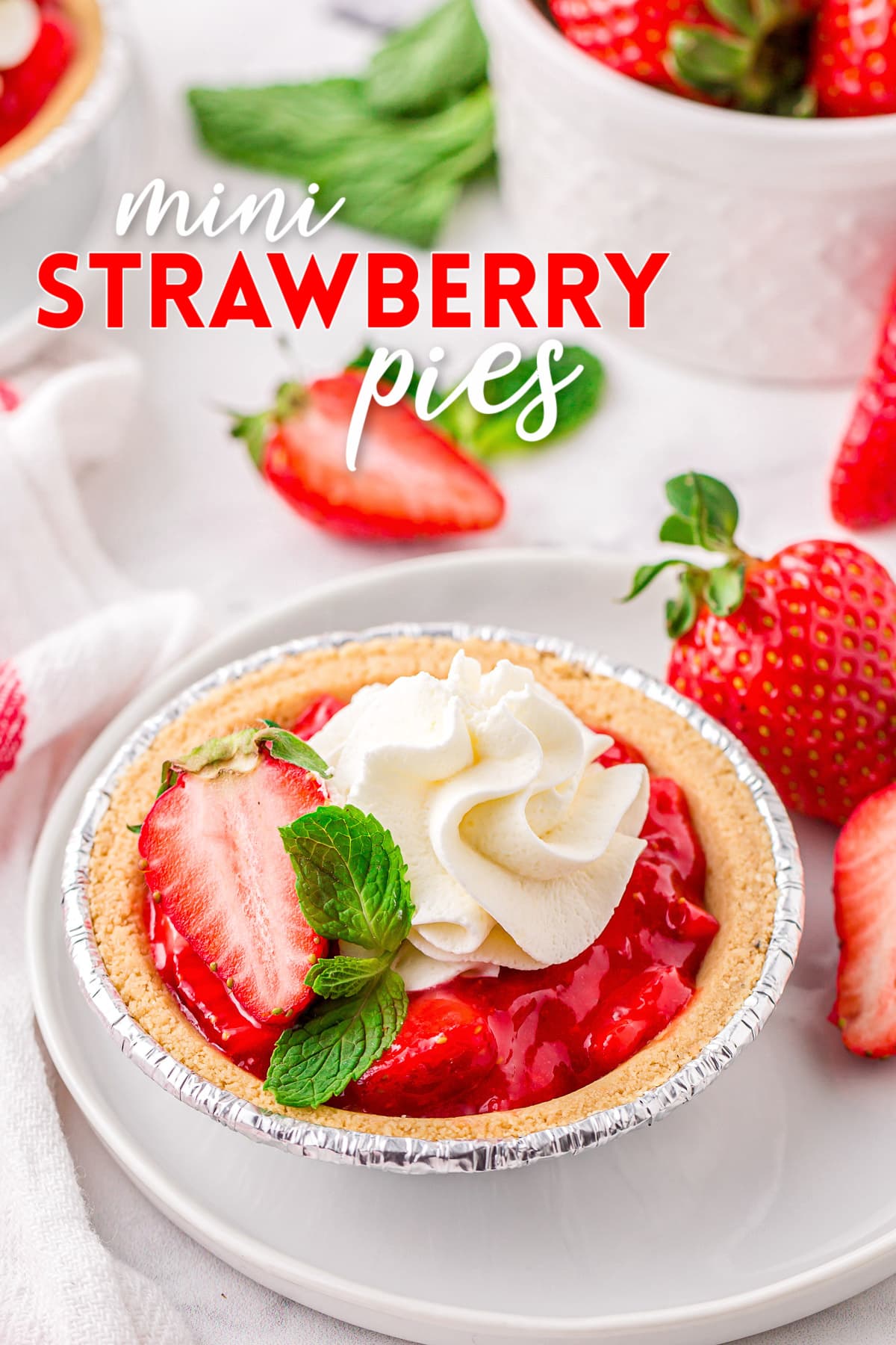 easy fresh strawberry pie recipe made in mini graham cracker crusts topped with whipped cream and a mint leaf. title overlay at top of image.