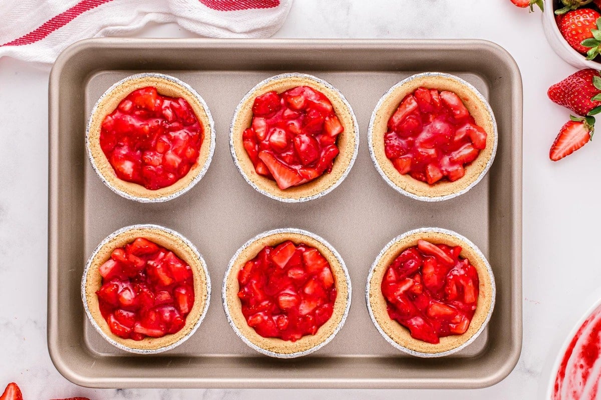 strawberry filling in six mini graham cracker crusts on sheet pan.