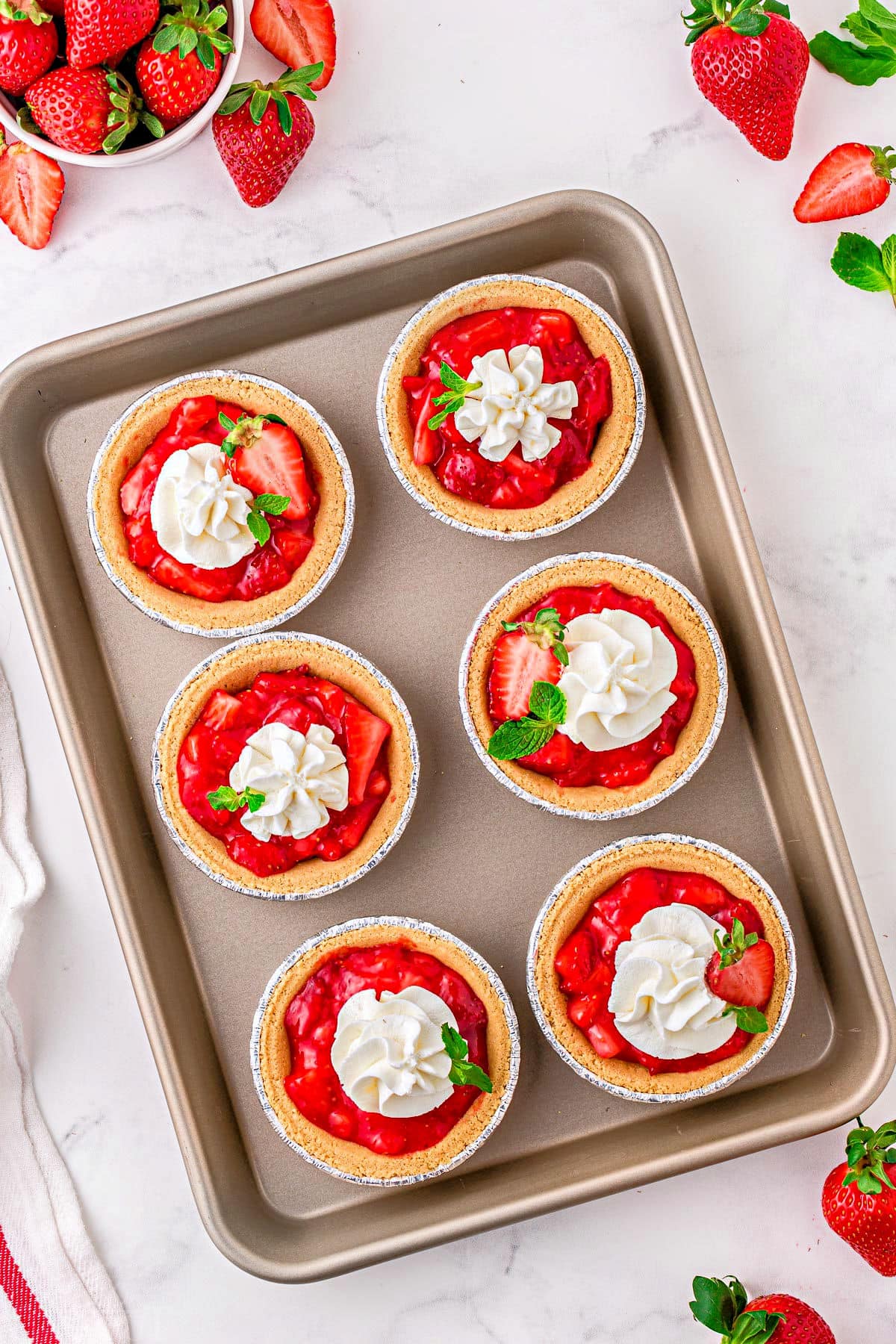 six mini strawberry pies on a baking sheet.